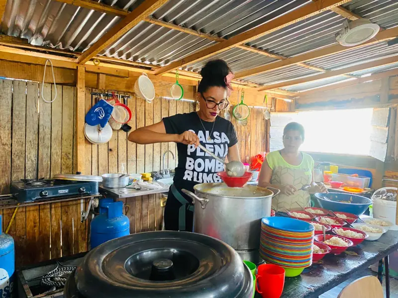 Dos mujeres cocinando en la cocina de madera del comedor, con ollas grandes y platos listos
