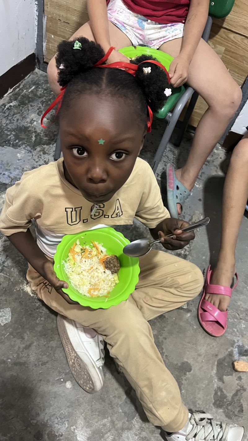 Una niña almorzando arroz en un plato verde, sentada en el comedor