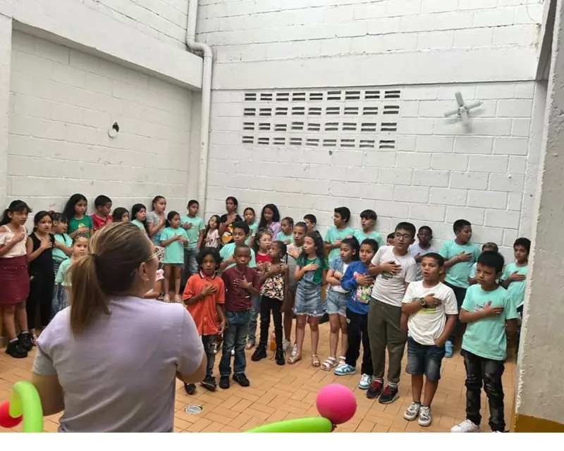 Una voluntaria dirigiendo a un grupo grande de niños de pie en un patio