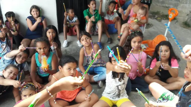 Niñas y niños sentados en el piso mostrando palitos de colores