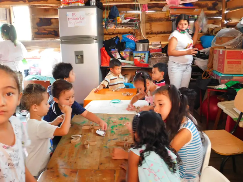 Niños pintando en una mesa, en un salón con paredes de madera