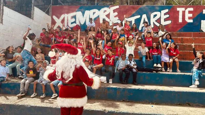 Papá Noel saludando frente a los niños sentados en las graderías