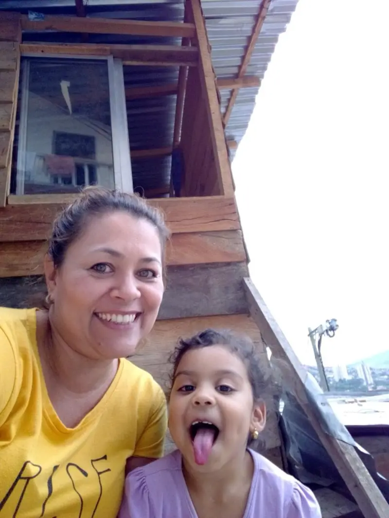 Una voluntaria y una niña sacando la lengua en una selfie frente a la casita de madera
