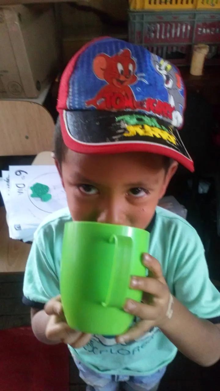 Niño con gorra tomando de un vaso verde