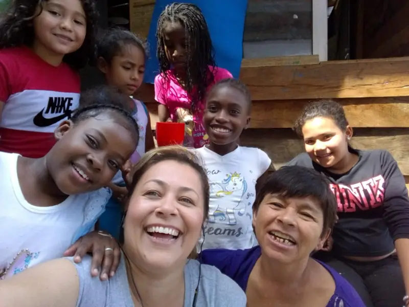 Selfie de dos voluntarias rodeadas de niñas sonrientes