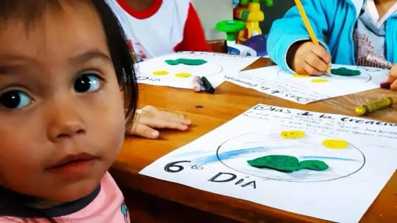 Niña pequeña mirando a la cámara junto a una hoja de actividades