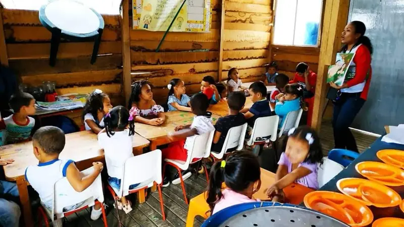 Niños sentados en mesas con platos naranjas en el salón de madera del comedor