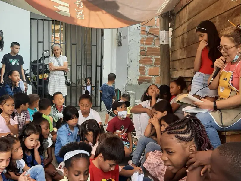 Una voluntaria leyendo con micrófono a niños sentados en el piso
