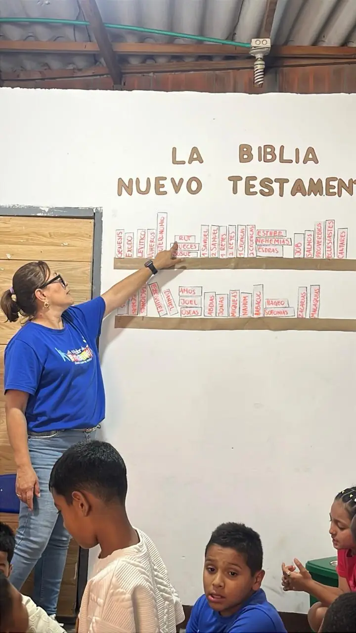 Una voluntaria señalando un mural de los libros del Nuevo Testamento frente a los niños