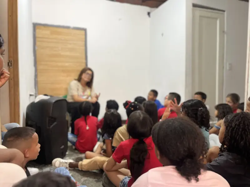 Niños sentados en el piso escuchando a una maestra en el salón del comedor