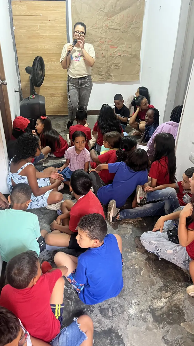 Niños sentados en el piso del salón escuchando a una voluntaria