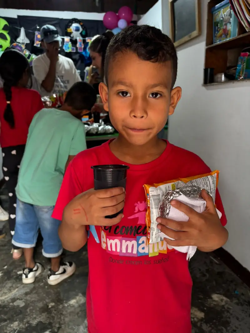 Niño con camiseta roja del comedor sosteniendo un vaso y su merienda