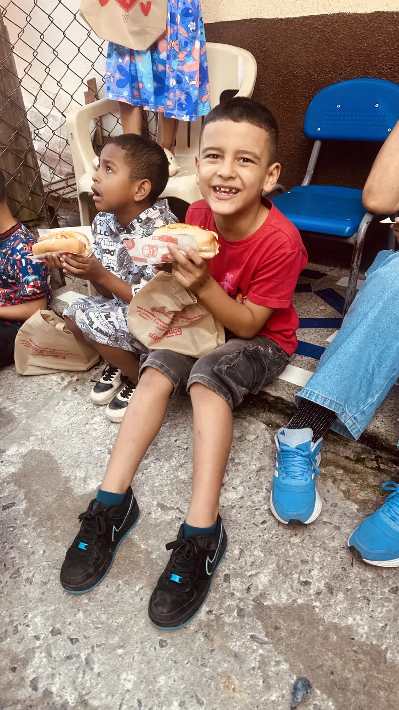 Niño con camiseta roja comiendo pan, sentado junto a otros niños