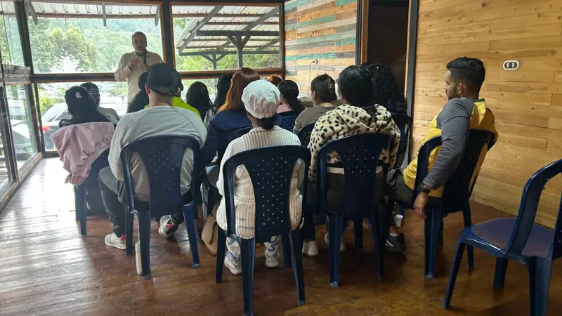 A group of people seated listening to a man in a room with wooden walls