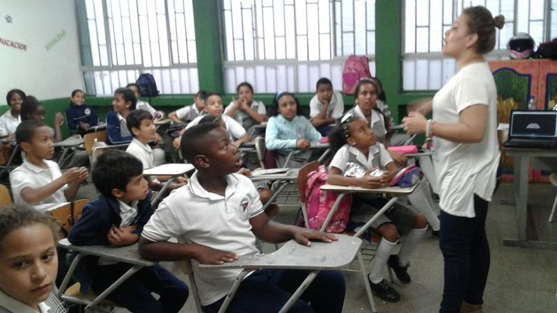 Children in school uniforms in a classroom, listening to a teacher