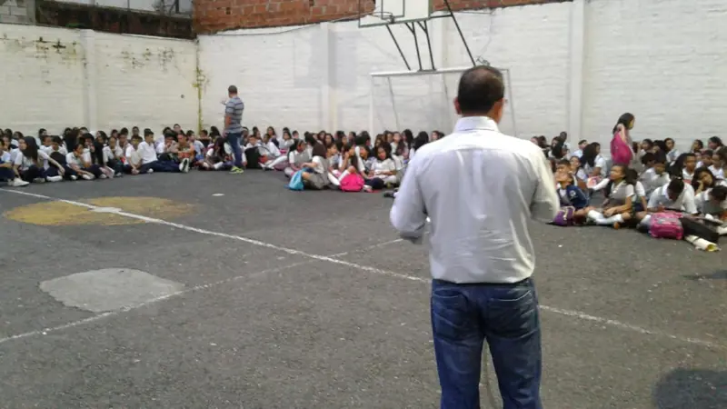 A man speaking to students seated in a school yard