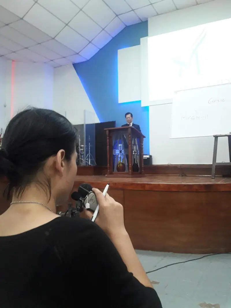 A participant taking notes while a preacher speaks from the pulpit