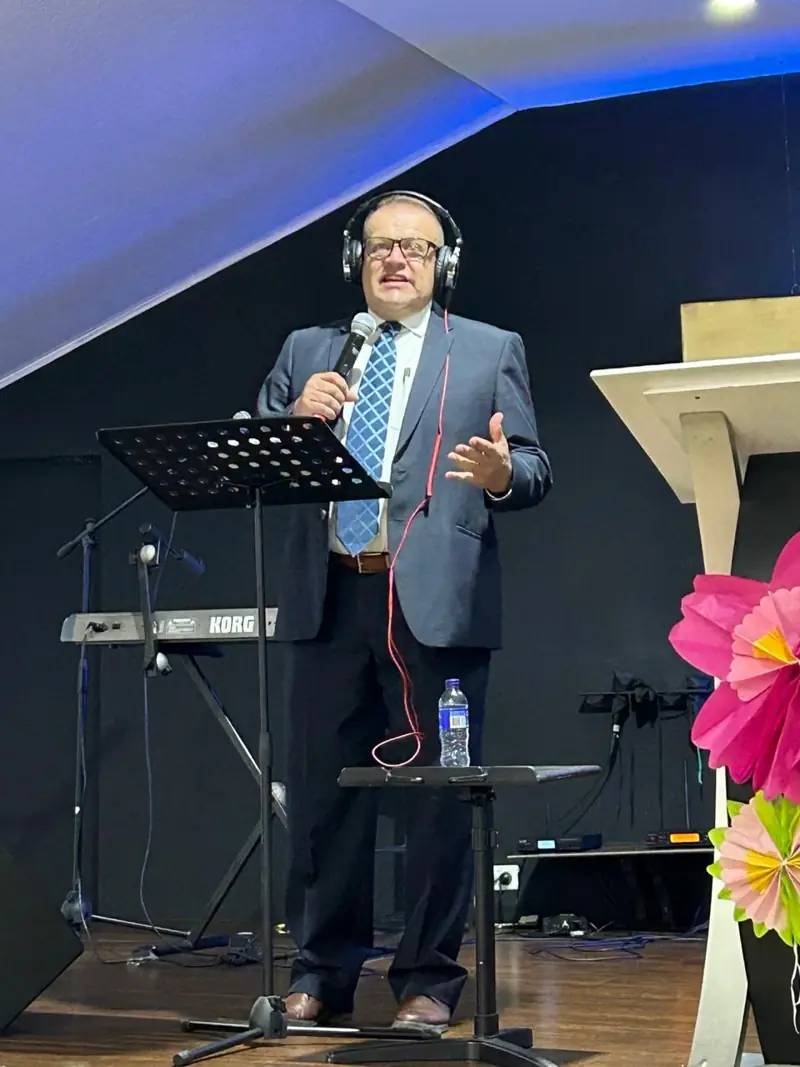 A preacher speaking with a microphone on a stage next to a music stand