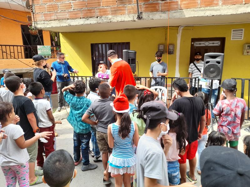Voluntarios del Centro con niños y familias frente a una casa amarilla durante una celebración de Navidad en el barrio